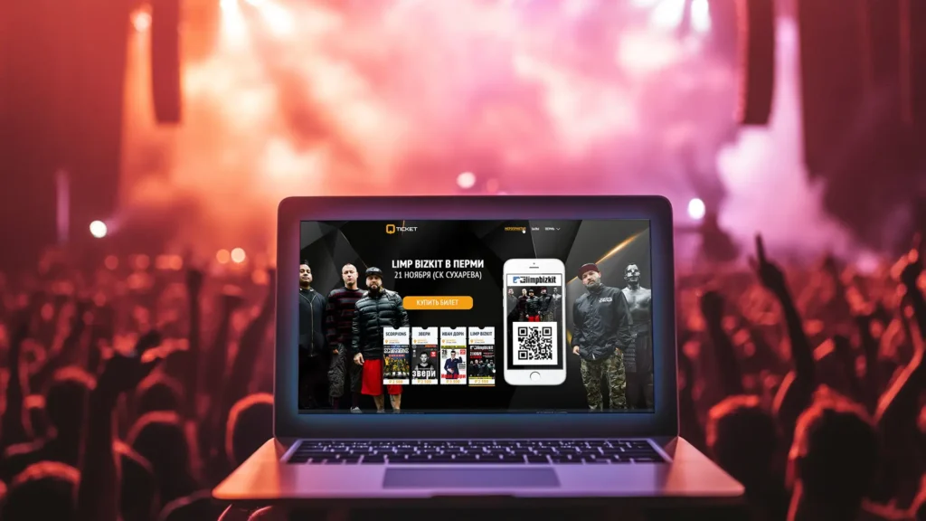 Ноутбук с открытым сайтом QTicket на фоне концертной сцены с освещённой толпой